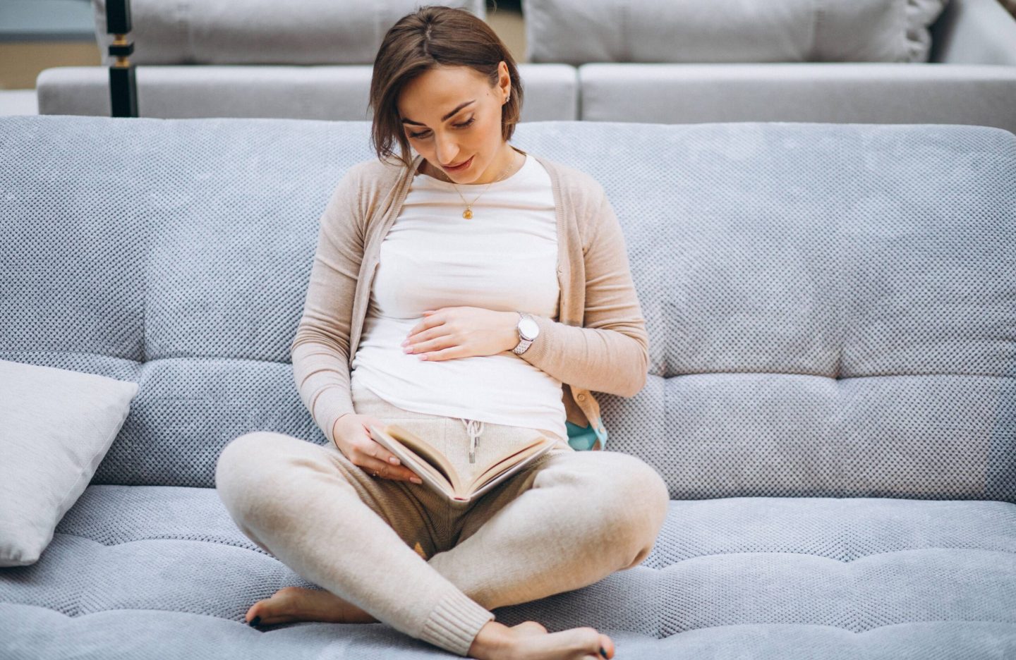 Young pregnant woman reading a book at home